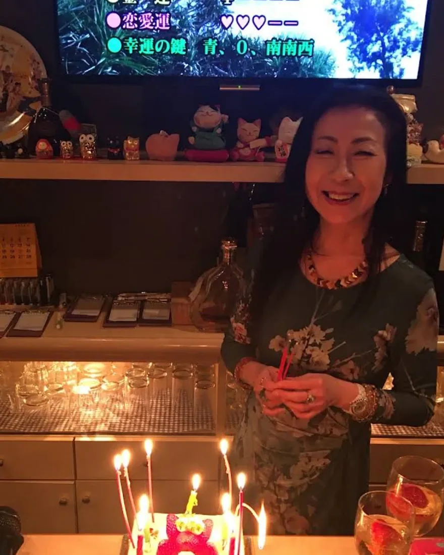笑顔の女性。手前に、ろうそくの灯ったケーキが見える。