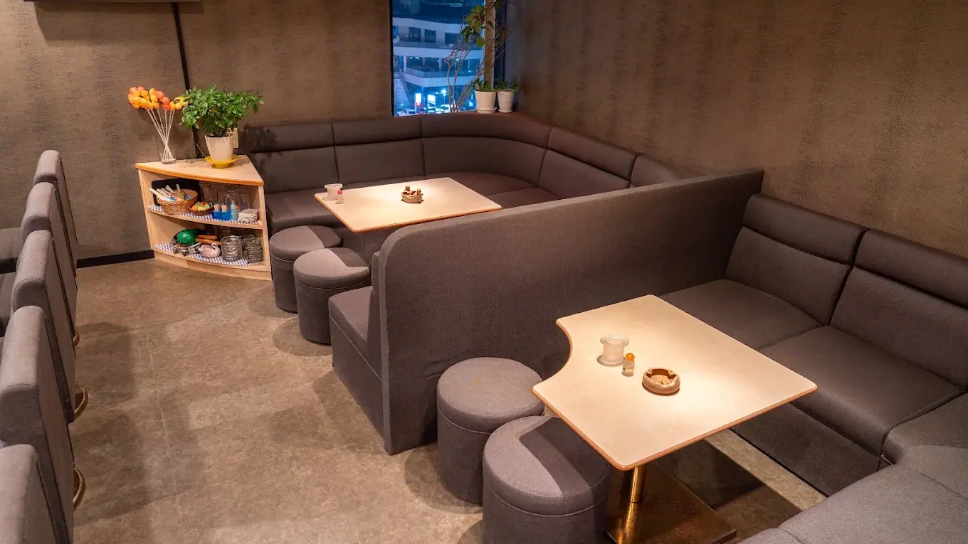 カウンター席の奥に、ソファ席とテーブルが並ぶ店内。窓の外に夜の街の明かりが見える。